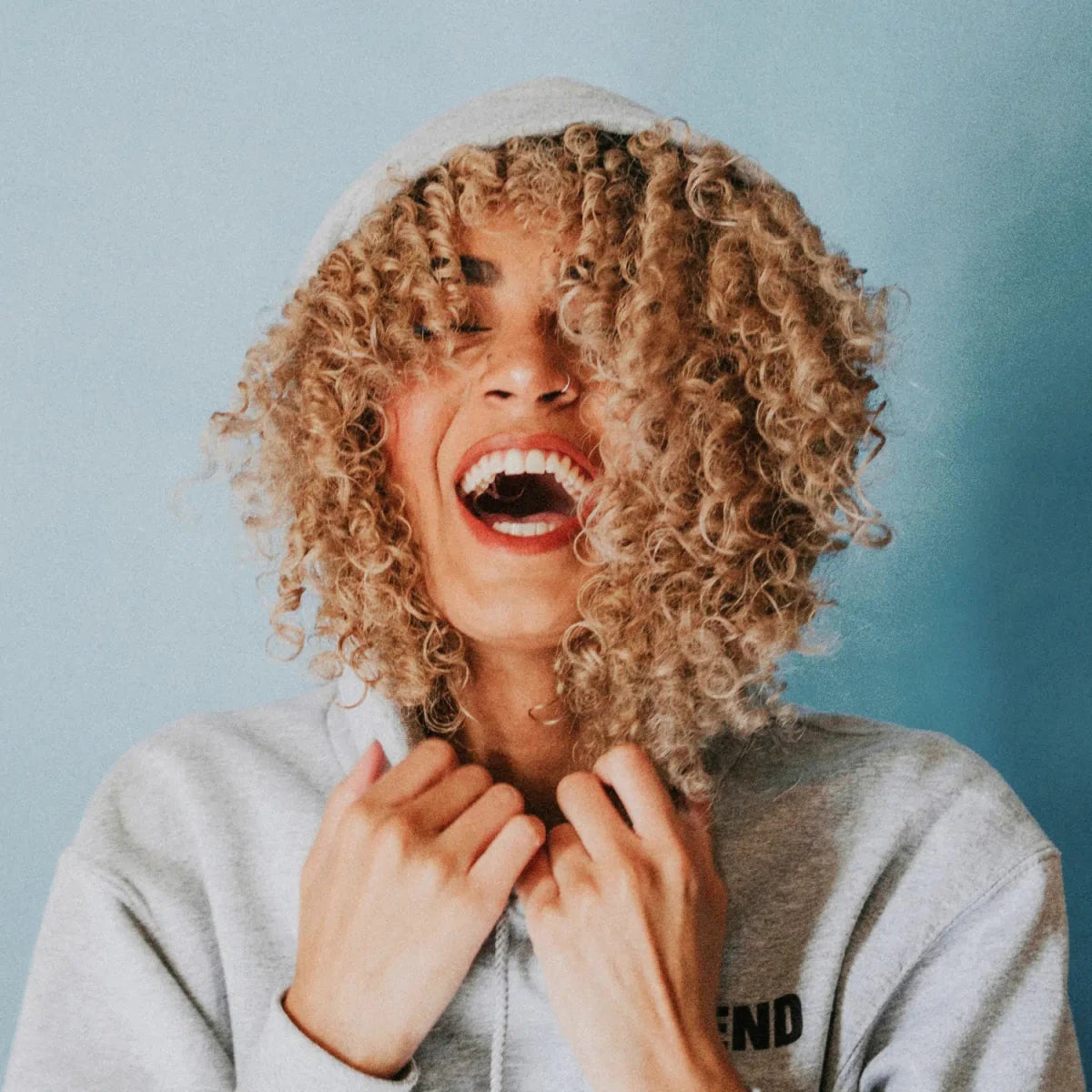 Biotin and Hair Vitamins: Laughing woman, full curls under hood