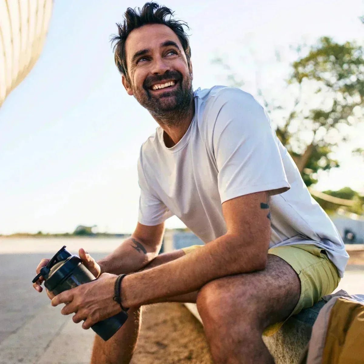 Mann mit Shaker sitzt am Straßenrand und lacht