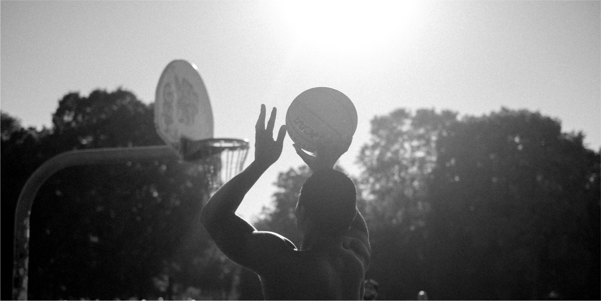 A man catches a frisbee on a basketball court, surrounded by natural elements.