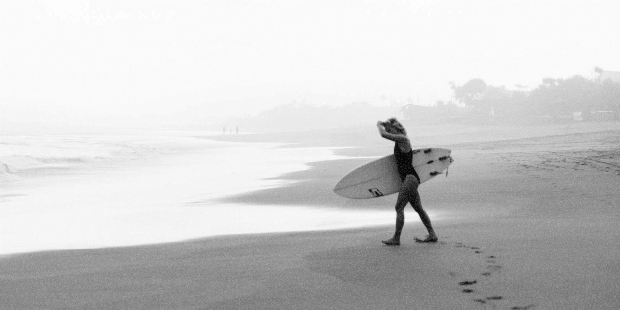 A person walking on the beach with a surfboard, surrounded by natural elements.